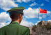China Grabbed 220M Voters — Now What? Soldier in a green military uniform facing the Great Wall of China with the Chinese flag in the background