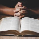 28,551 Dead—But Not ‘Genocide’? Hands clasped over an open book on a wooden table