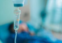 Why America Outsources Ebola Care Close-up of an IV drip in a hospital setting with a patient in the background