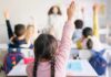 Parents Misled As Red Ink Surges Students in a classroom raising their hands to answer a question