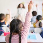 Students in a classroom raising their hands to answer a question