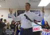 Wuhan Fix? FBI Blocks Airport Grill man in white shirt speaking at a rally with supporters and signs behind him