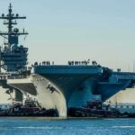 Trump’s Bridge Rule Escalates Fast Aircraft carrier guided by tugboats in a harbor