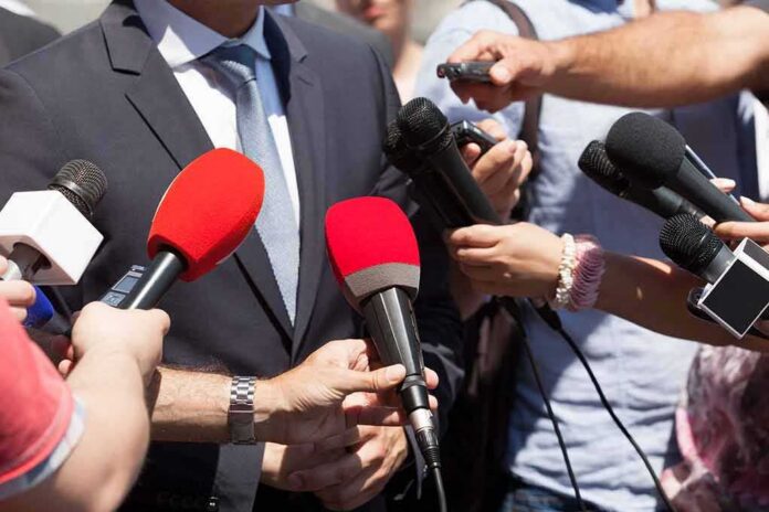 shutterstock_1042717348 Person in suit surrounded by microphones during media interview