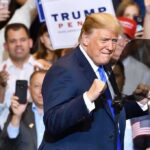 man in suit raising fists at a rally podium