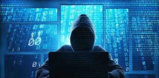 Hooded figure using a laptop in front of glowing code