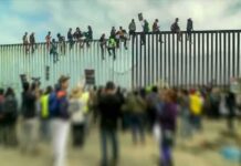 DSA Leader Endorses Amnesty, ICE Axe People sitting atop a tall border fence during a gathering