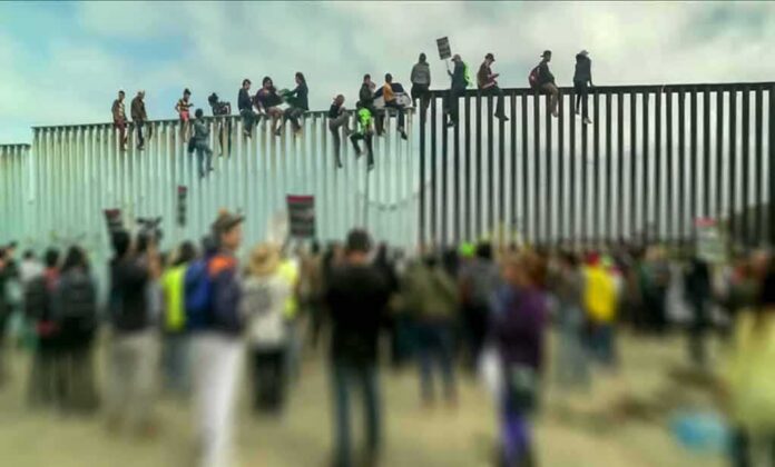 People sitting atop a tall border fence during a gathering