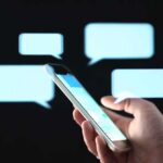 Hand holding smartphone with chat bubbles on dark background