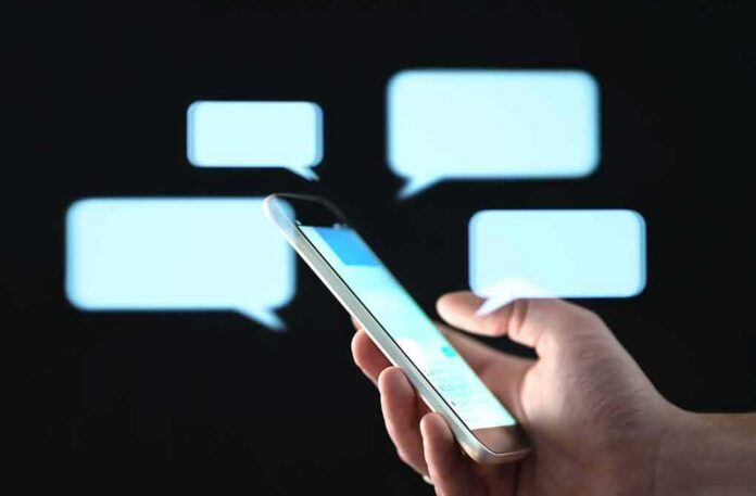 shutterstock_1452139727 Hand holding smartphone with chat bubbles on dark background