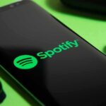 Smartphone showing Spotify app logo with wireless earbuds nearby