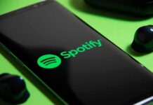 Smartphone showing Spotify app logo with wireless earbuds nearby