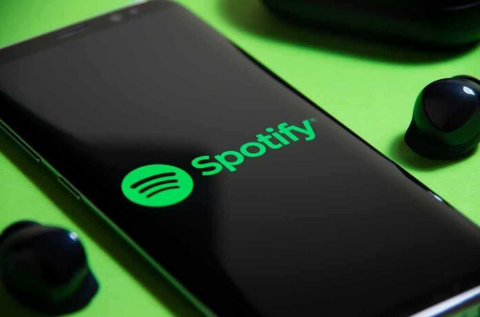 Smartphone showing Spotify app logo with wireless earbuds nearby