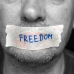 A mans mouth is covered with a piece of tape that has the word FREEDOM written on it