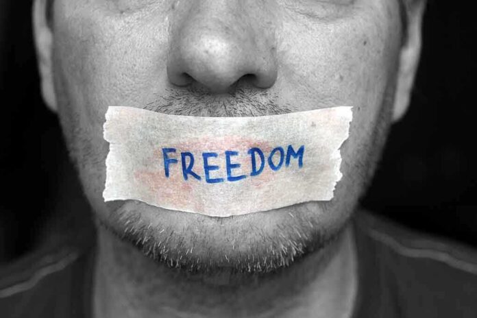 shutterstock_187662866 A mans mouth is covered with a piece of tape that has the word FREEDOM written on it