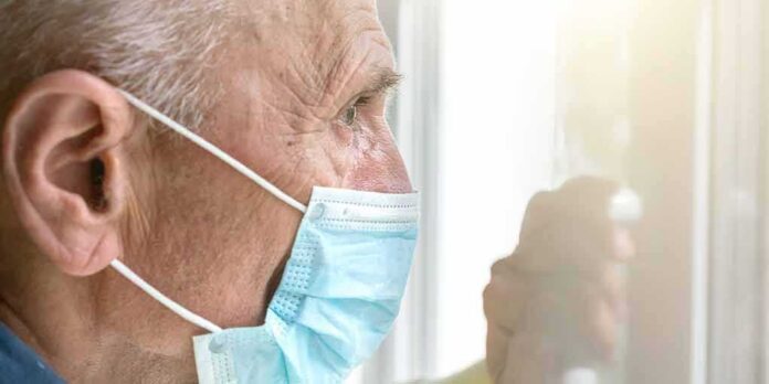 Older man wearing a surgical mask looking out a window