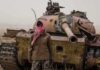 Nationwide Uprising Rumors Rattle Kabul Man in scarf stands before a rusted tank in a barren field