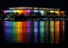 Modern building lit in rainbow colors reflected on water at night