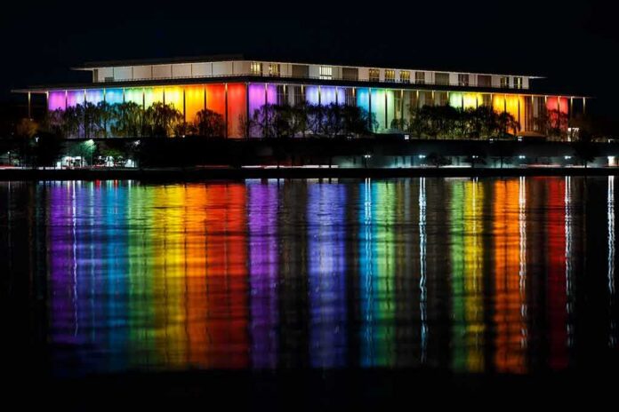 Modern building lit in rainbow colors reflected on water at night