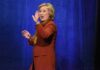 Cathedral Send-Off Teased—Clinton Whispers woman in orange coat gesturing on stage