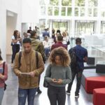 Students walking through a bright campus atrium using mobile devices
