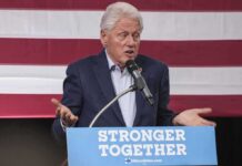 man speaking at a podium with an American flag backdrop