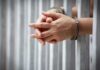 DHS Fumes: Murderer Back On Streets hands in handcuffs behind jail bars