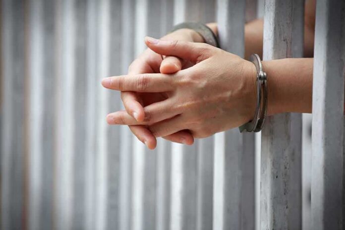shutterstock_1031018551 hands in handcuffs behind jail bars