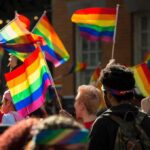 Bear Pascoe at a pride parade holding a rainbow flag among a cheering crowd