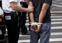 Teen Arrested After Beverly Hills Bloodshed police officer detains person with hands zip-tied behind back