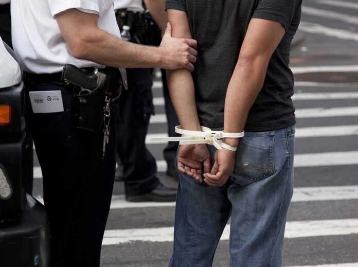 shutterstock_113188777 police officer detains person with hands zip-tied behind back