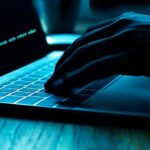Hand typing on laptop with green code on screen