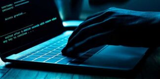 Hand typing on laptop with green code on screen