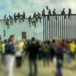 People sitting atop a tall border fence during a protest