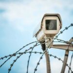 Security camera above barbed wire against blue sky