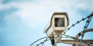 Security camera above barbed wire against blue sky