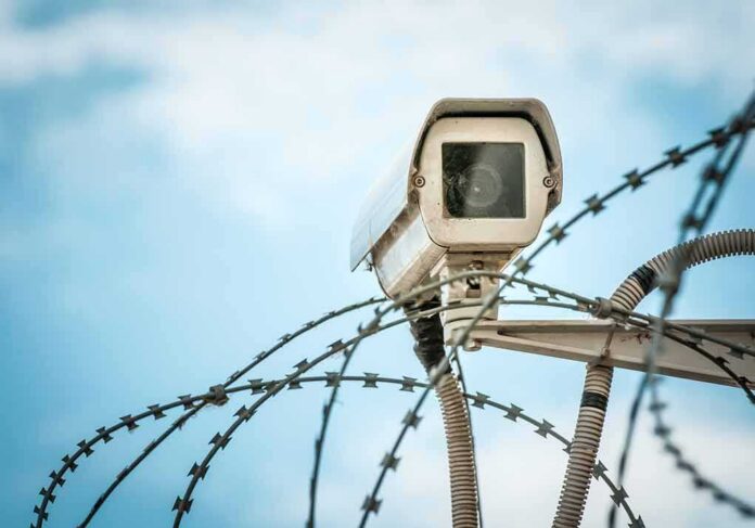 shutterstock_132392237 Security camera above barbed wire against blue sky