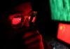 person wearing glasses with reflections of a red flag and computer screens