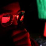 U.S. Troops Killed – China Imagery Tied To Deadly Strike person wearing glasses with reflections of a red flag and computer screens