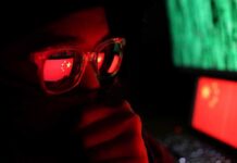 person wearing glasses with reflections of a red flag and computer screens
