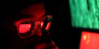 person wearing glasses with reflections of a red flag and computer screens
