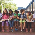 children sitting on a brick ledge reading books