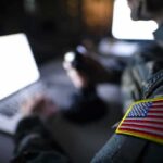 Soldier with U.S. flag patch using a laptop in a dim room