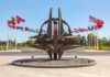 Kyiv – Warsaw Line Hit Steps From NATO Metal sculpture with surrounding national flags in a plaza