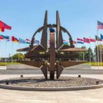 Kyiv – Warsaw Line Hit Steps From NATO Metal sculpture with surrounding national flags in a plaza