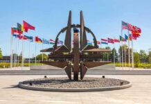 Kyiv – Warsaw Line Hit Steps From NATO Metal sculpture with surrounding national flags in a plaza