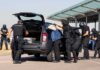 customs officers detain a person beside a car with its trunk open