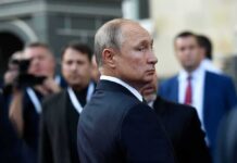Vladimir Putin in a dark suit looking over his shoulder amid a crowd