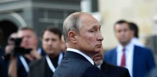 Vladimir Putin in a dark suit looking over his shoulder amid a crowd