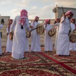 Hormuz Showdown: Qatar Plays Power Broker Jonathan Cyprien among traditional drummers in white thobes performing outdoors